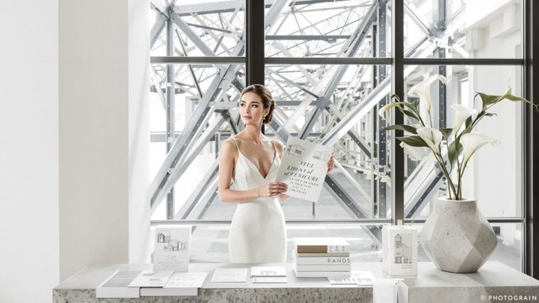 Bride in elegant wedding dress holding a magazine in modern industrial venue.