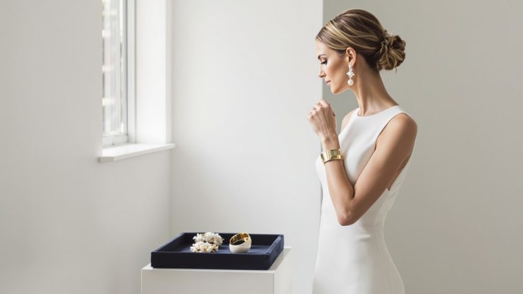 Elegant bride in white dress looking out window, bridal jewelry, minimalistic setting.