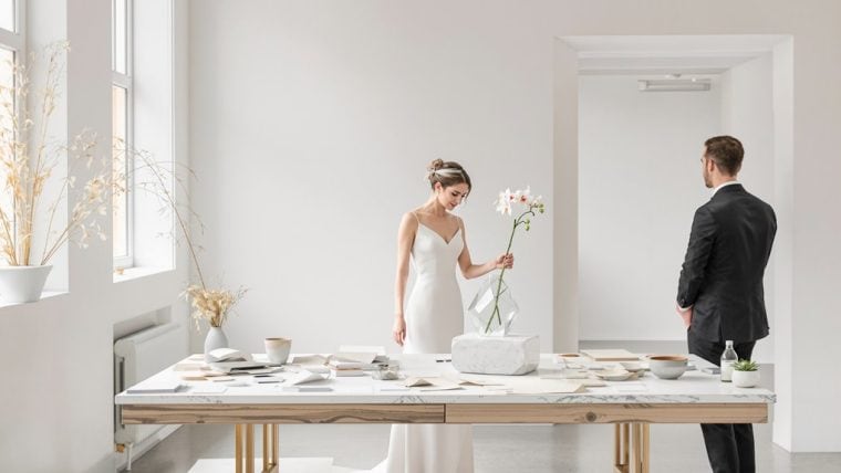 Elegant wedding ceremony with bride holding a flower and groom waiting, set in a bright, minimalist.