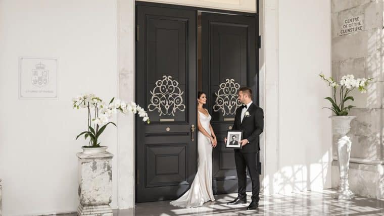 Bride and groom outside historic venue with elegant black doors and floral decor.