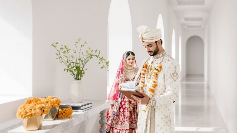 Indian groom in sherwani and turban, bride in red bridal lehenga with jewelry.
