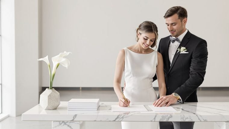 Happy bride and groom signing wedding registry at modern reception desk.