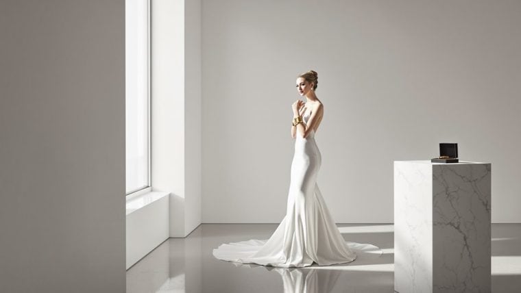 Bride in elegant white wedding gown standing in bright minimalist room.