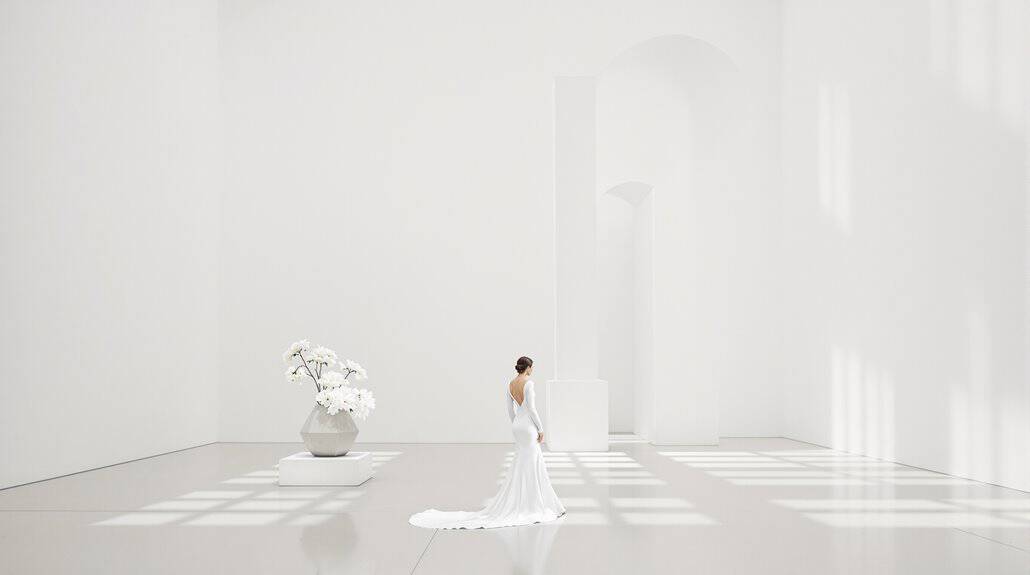 Elegant wedding bride in white gown standing in a bright, minimalist venue with natural light.