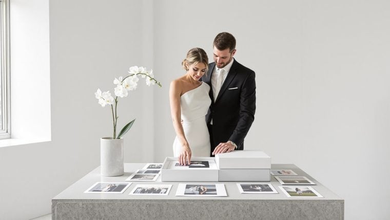 Elegant wedding couple viewing photo album at a modern gallery table.