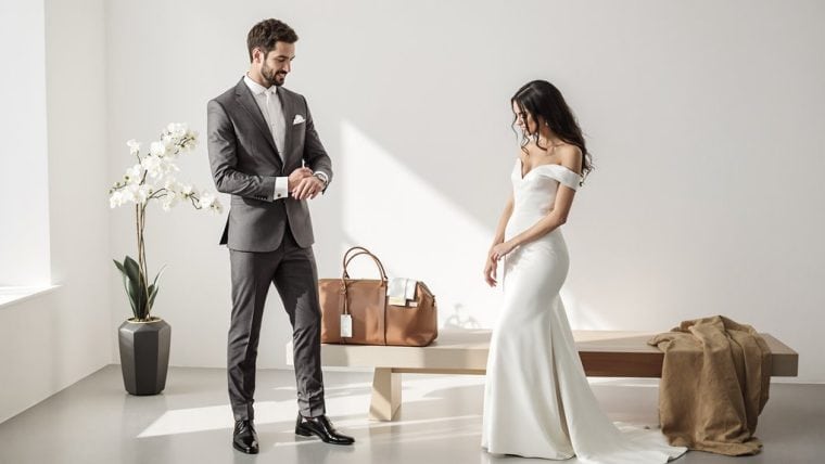 Bride in elegant white wedding gown and groom in tailored gray suit with bow tie.